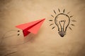 Red paper airplane flying next to hand drawn light bulb on beige background, symbolizing creativity and innovation