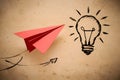 Red paper airplane flying next to hand drawn light bulb on beige background, symbolizing creativity and innovation