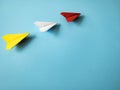 Red paper airplane origami leading white and yellow airplanes on blue background with customizable space for text Royalty Free Stock Photo