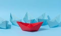 A red paper boat stands in front of a group of blue paper boats, a confrontation