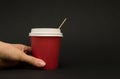 Red paper cup for coffee with a lid on a black background, hand is holding a paper cup