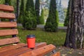 A red paper cup with coffee stands on an empty wooden bench in an autumn park. Autumn landscape with fallen leaves Royalty Free Stock Photo