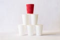 Red paper cup stands on top of white paper cups pyramid