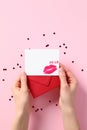 Red paper envelope with blank white note mockup in female hands over pink background with Valentines hearts confetti. Romantic Royalty Free Stock Photo