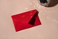 Red paper envelope and sparkling mirror ball on beige background with light reflections and shadows, aesthetic minimal