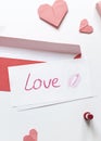 Red paper envelope with white blanks, word love written with red lipstick and pink origami hearts.