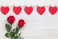 Red paper heart hanging on brown nature rope with mini clothespin and rose flower. On white wooden plank. For Valentine day and l Royalty Free Stock Photo