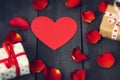 Red paper heart with rose petals and gifts on a dark wooden background. St. Valentine`s Day. Royalty Free Stock Photo