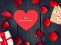 Red paper heart with rose petals and gifts on a dark wooden background. St. Valentine`s Day. Royalty Free Stock Photo