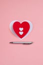 Red paper heart with a silver pen on the pink background. Valentine`s or Wedding`s day postcard concept.