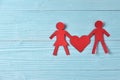 Red paper people holding heart on blue wooden background. Royalty Free Stock Photo