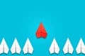 Red paper plane flying in front of a group of whites. Blue background. Copy space. Leadership concept, teamwork, personnel