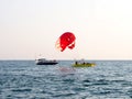 A red parachute is tied to a yellow pleasure boat at sea. Marine entertainment. Seasonal cruise boat trips