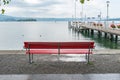 Red park bench on a lake shore with a view of the harbor pier Royalty Free Stock Photo