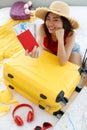 Red passport with air flight tickets in hands of Asian young female traveler wears big hat sitting look at camera packing personal Royalty Free Stock Photo