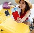 Red passport with air flight tickets in hands of Asian young female traveler wears big hat sitting look at camera packing personal Royalty Free Stock Photo