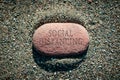 Red pebble stone alone on sand with words Social Distancing carved on it
