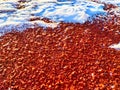 Red pebbles or rubberized textured material and white snow on it. Background, texture, frame, copy space. Contrast of