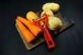 Red Peeler with peeled carrots and potatoes isolated on dark/black background