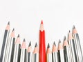 Red pencil standing out from crowd of black pencils against white background. Royalty Free Stock Photo