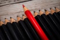 Red pencil stands out from the crowd of black on a wooden white background. Royalty Free Stock Photo