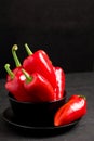 Red peppers in plate on black background - closeup photo of whole fresh ripe sweet vegetables in modern dark mood style for