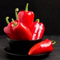 Red peppers in plate on black background - closeup photo of whole fresh ripe sweet vegetables in modern dark mood style for