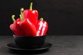 Red peppers in plate on black background - closeup photo of whole fresh ripe sweet vegetables in modern dark mood style for