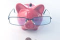 A red piggy bank with glasses stands on the table with a coin in front of it. View from above Royalty Free Stock Photo