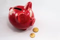 Red Piggy bank on a white table. Coin box with euro coins lying nearby. The concept of saving or save money or open a bank deposit