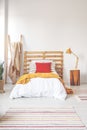 Red pillow and orange blanket on comfortable teenager bed with white bedding in elegant oldschool bedroom interior with copy space Royalty Free Stock Photo