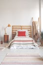 Red pillow on single bed with striped bedding in spacious bedroom interior, real photo with copy space on the empty wall Royalty Free Stock Photo