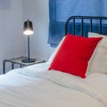 red pillow on white bed with blue curtain and black lamp on table side
