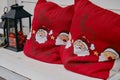 Red pillows with Santa's head and the inscription merry Christmas on a white wooden bench. Decorative lantern with