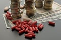 Red pills or capsules against dollar bills and stacks of coins Royalty Free Stock Photo