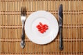 Red pills on white plate with fork and knife on table