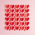 Red and pink paper hearts are arranged in a grid pattern on a light pink background. Th Royalty Free Stock Photo