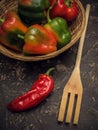 Red pipper and wodden fork on stone table in kitchen, with basket of green peppers