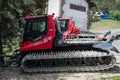 Red PistenBully 600 W snow groomer parked near a green tree and a building on a sunny day Royalty Free Stock Photo