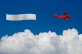 Red plane pulls blank banner above white clouds Royalty Free Stock Photo