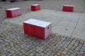 Red plastic benches in the shape of blocks with handles. The square is paved with granite cubes. sandy surface. built around a squ