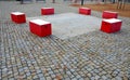 Red plastic benches in the shape of blocks with handles. The square is paved with granite cubes. sandy surface. built around a squ