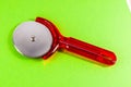 A red plastic pizza cutter sits on a green background Royalty Free Stock Photo