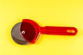 A red plastic pizza cutter sits on a yellow background Royalty Free Stock Photo