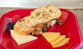 Red, plastic plate with samples of crusty bread, several selections of cheeses, blackberries, raspberries, strawberries