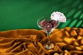 Red plastic poker chips lie in a glass margarita glass on a brown velvet cloth. A fan of small playing cards on the rim of a glass Royalty Free Stock Photo