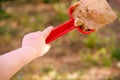 Red plastic scoop scoop in a children`s hand. Play in the sandbo