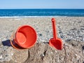 Red plastic shovel and bucket for children in the sand on the beach in front of the sea Royalty Free Stock Photo