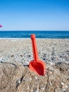 Red plastic shovel for children stuck in the sand on the beach in front of the sea Royalty Free Stock Photo