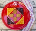 A red plate is decorated with a square made of triangular slices of bread on which fruit jam has been spread